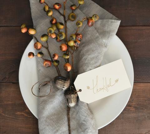 White plate with linen napkin and seasonal dried berries tied with note that says Thankful