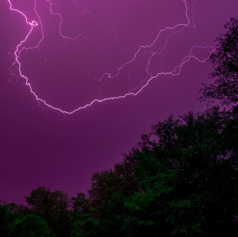 April '21 photo writing prompt_image of lightning against dark purplish sky over darkened trees