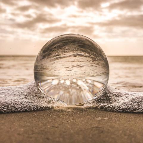 air bubble in foam in a beach shore reflecting both sea and dawn sky via Canva