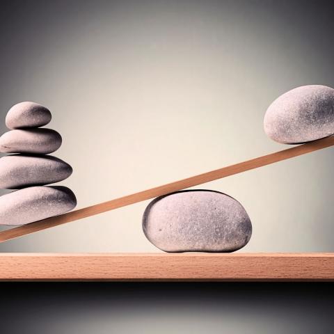 wooden seesaw balancing one larger stone with several smaller ones