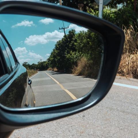 closeup of a black car's side view mirror reflection the road behind the car via Canva