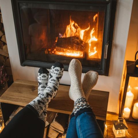 two pairs of outstretched legs with thick socks in front of a fireplace via Canva