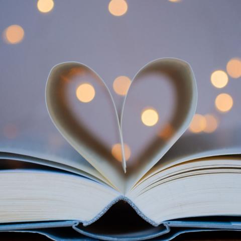 an open book with pages folded in to resemble a heart and twinkling lights in the background via canva