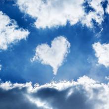photo of a heart shaped cloud in a blue partly cloudy sky with bright sun via Canva