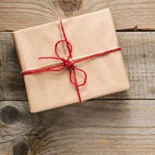 square gift box wrapped in brown paper tied with red string on wooden surface