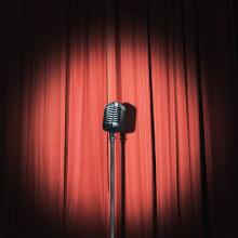 spotlight on a microphone on stand in front of a red curtain via Canva